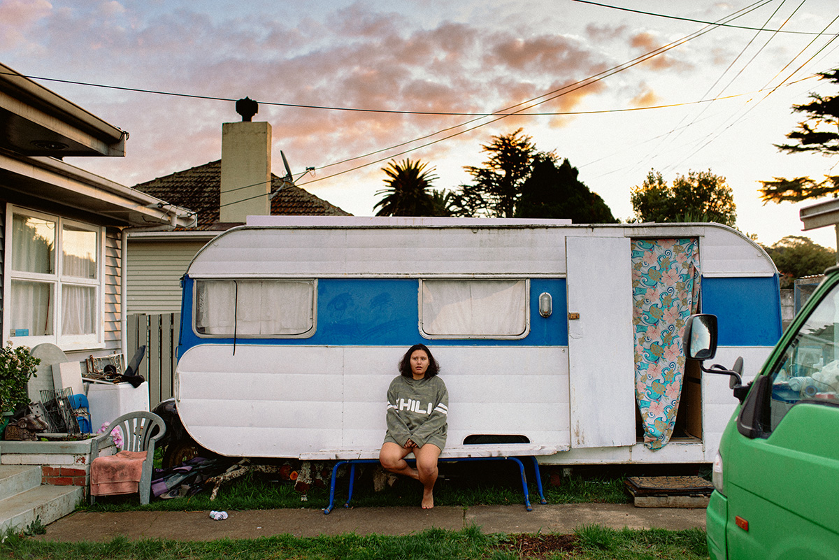 Sophie in a jumper, sitting in front of a caravan with pink clouds in the sky as the sun sets