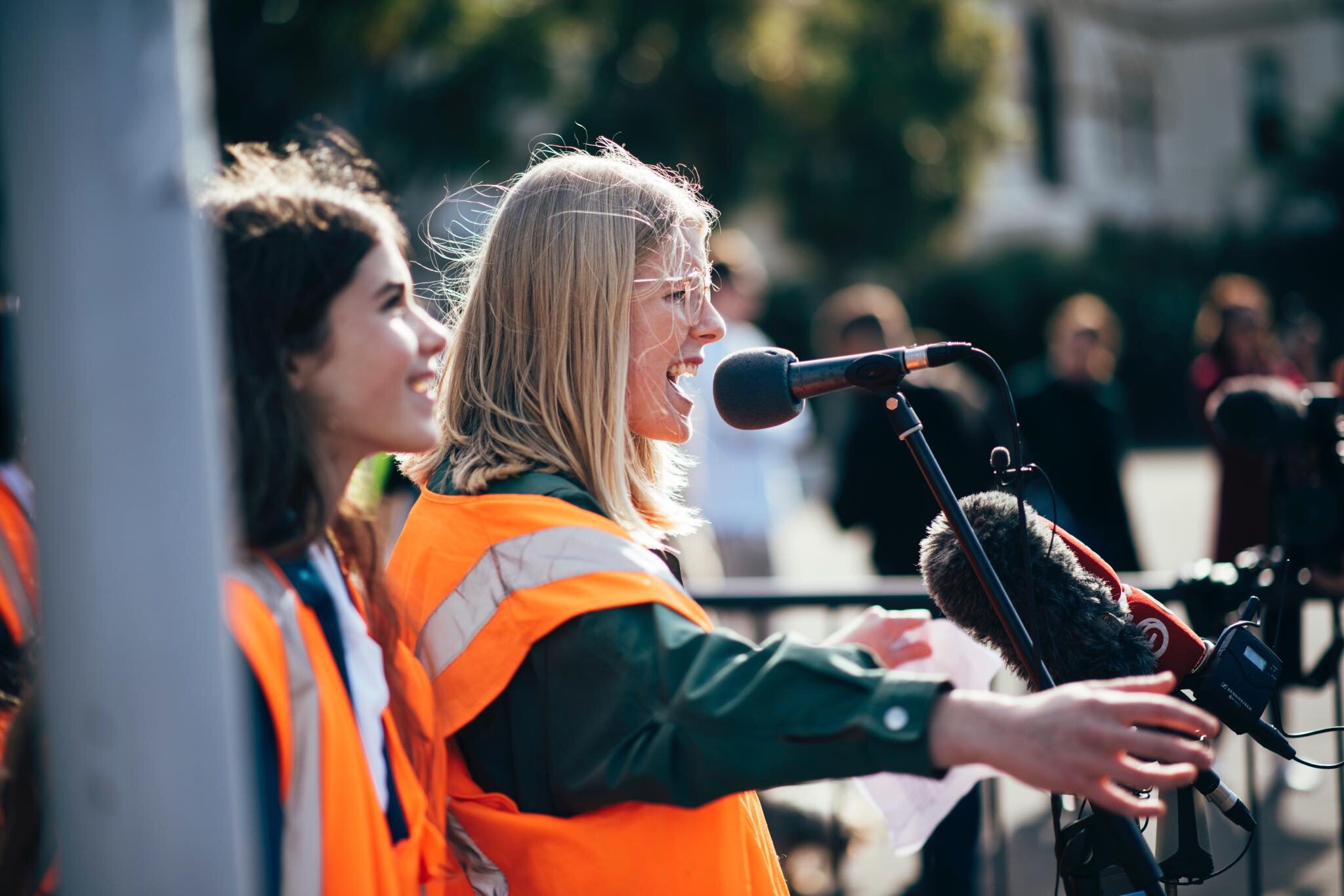 Young woman wearing high vis vest speaking to crowd